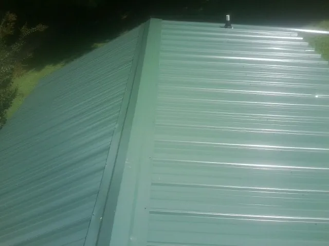 New green metal panels meeting at the ridge of a roof — Flat Roof Repair work by our crew in Milan